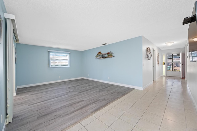 empty room with visible vents, baseboards, a textured ceiling, and light wood-style flooring