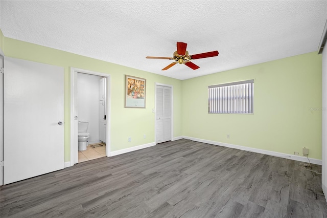 unfurnished bedroom with a textured ceiling, ensuite bath, wood finished floors, a closet, and baseboards