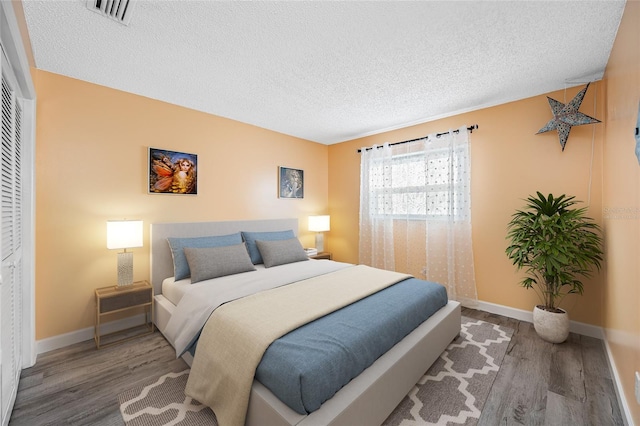 bedroom featuring visible vents, a textured ceiling, baseboards, and wood finished floors