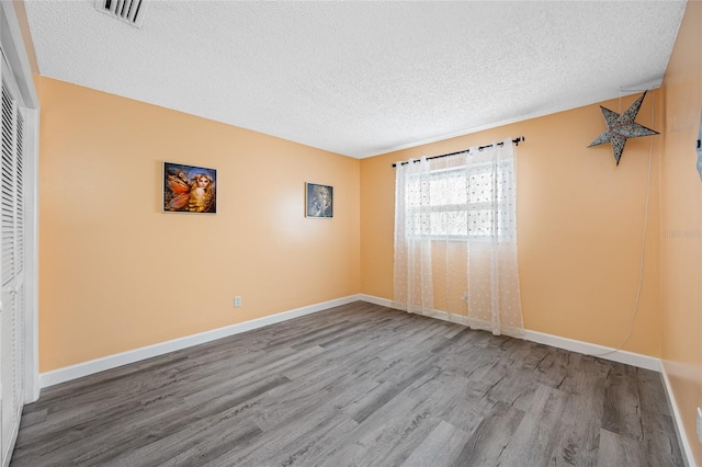 empty room with visible vents, baseboards, a textured ceiling, and wood finished floors