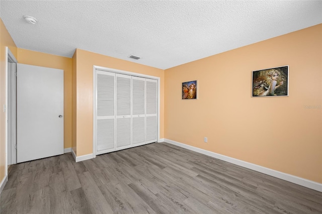 unfurnished bedroom with visible vents, baseboards, wood finished floors, a closet, and a textured ceiling