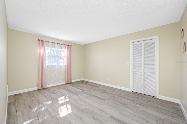 unfurnished bedroom with a closet, baseboards, a textured ceiling, and wood finished floors