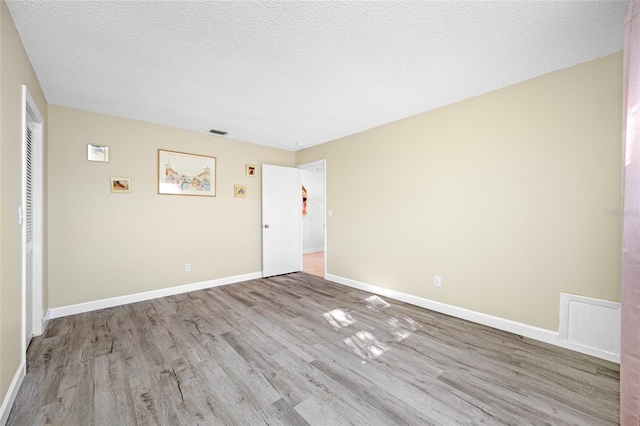 spare room featuring visible vents, baseboards, a textured ceiling, and wood finished floors