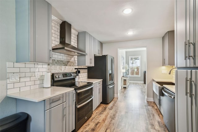 kitchen with tasteful backsplash, wall chimney range hood, gray cabinets, appliances with stainless steel finishes, and light wood-style floors