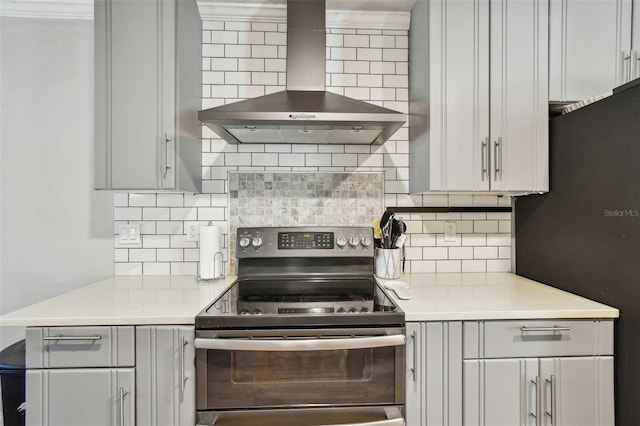 kitchen featuring double oven range, freestanding refrigerator, light countertops, wall chimney exhaust hood, and backsplash