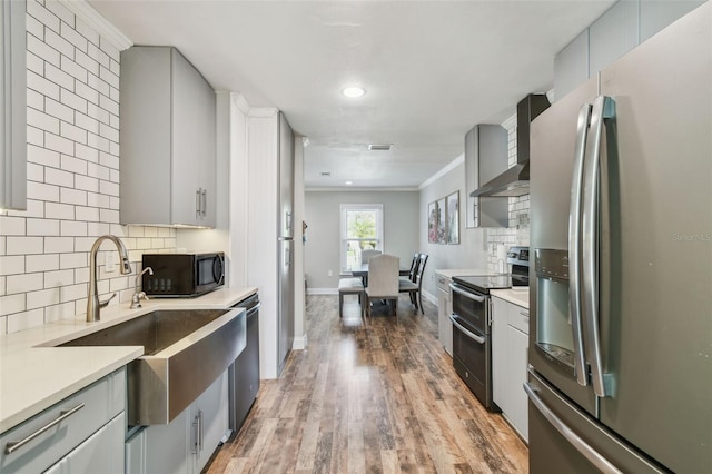 kitchen featuring wall chimney range hood, gray cabinets, appliances with stainless steel finishes, and a sink