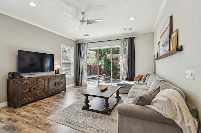 living room featuring visible vents, ceiling fan, baseboards, ornamental molding, and wood finished floors