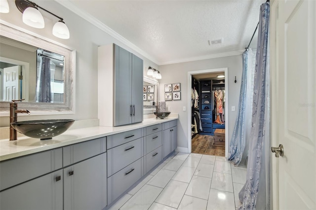 full bath with a sink, a textured ceiling, ornamental molding, and double vanity