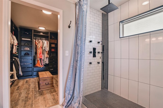 full bathroom featuring a tile shower, a spacious closet, and wood finished floors