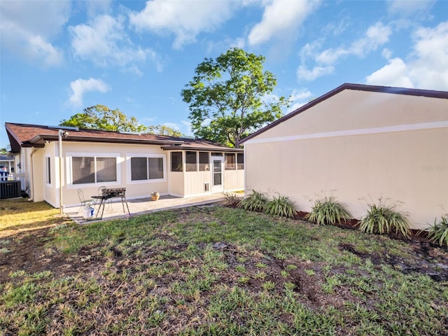 back of house featuring cooling unit, a sunroom, stucco siding, a patio area, and a lawn