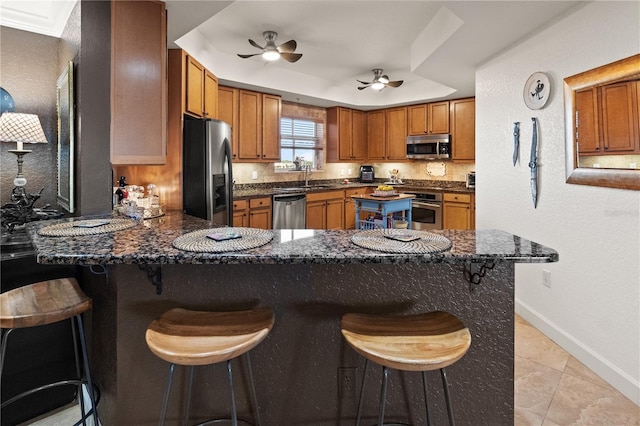 kitchen with brown cabinets, appliances with stainless steel finishes, a peninsula, a raised ceiling, and a sink