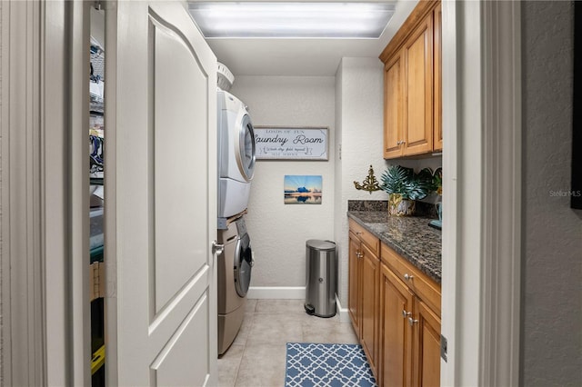 kitchen featuring brown cabinets, stacked washer and dryer, dark stone countertops, light tile patterned floors, and baseboards