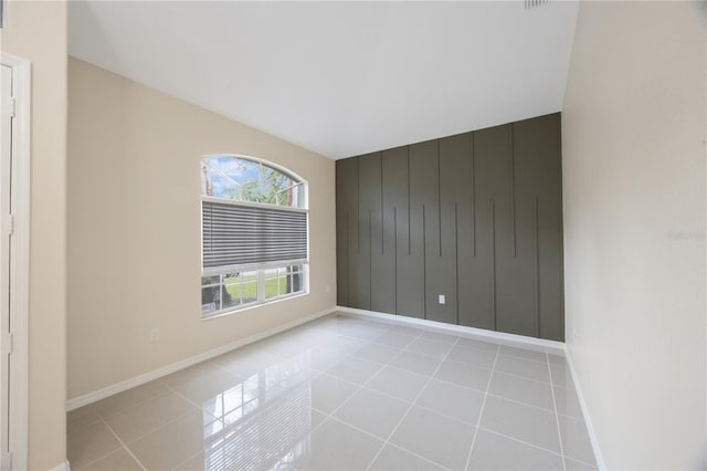 empty room with an accent wall, light tile patterned flooring, and baseboards