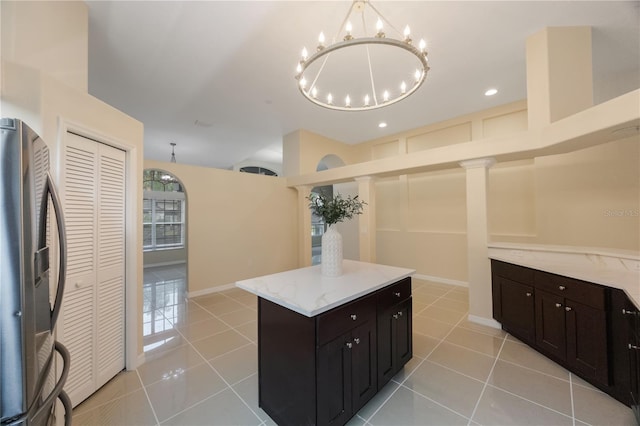 kitchen featuring a kitchen island, baseboards, light stone countertops, light tile patterned floors, and stainless steel fridge