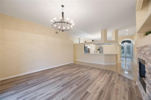 unfurnished living room with visible vents, baseboards, a stone fireplace, light wood-style floors, and an inviting chandelier