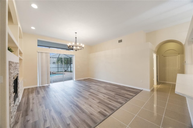 unfurnished dining area featuring visible vents, baseboards, a stone fireplace, recessed lighting, and wood finished floors