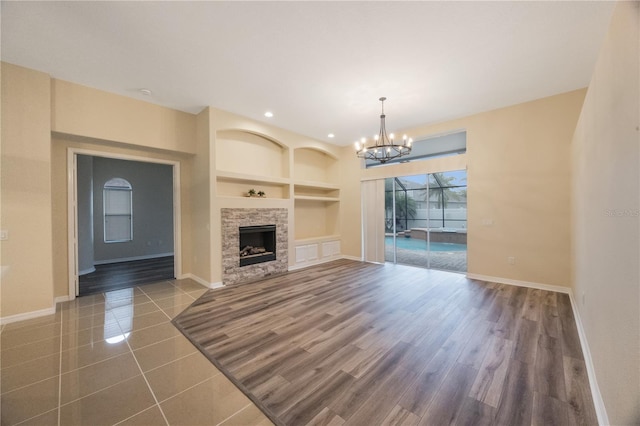 unfurnished living room featuring built in shelves, wood finished floors, baseboards, recessed lighting, and a stone fireplace