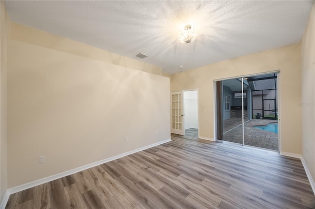 empty room featuring visible vents, wood finished floors, baseboards, and a textured ceiling