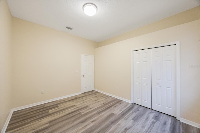 unfurnished bedroom with a closet, a textured ceiling, baseboards, and light wood-style floors