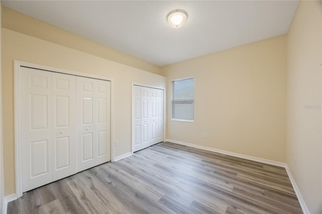 unfurnished bedroom featuring wood finished floors, multiple closets, and baseboards