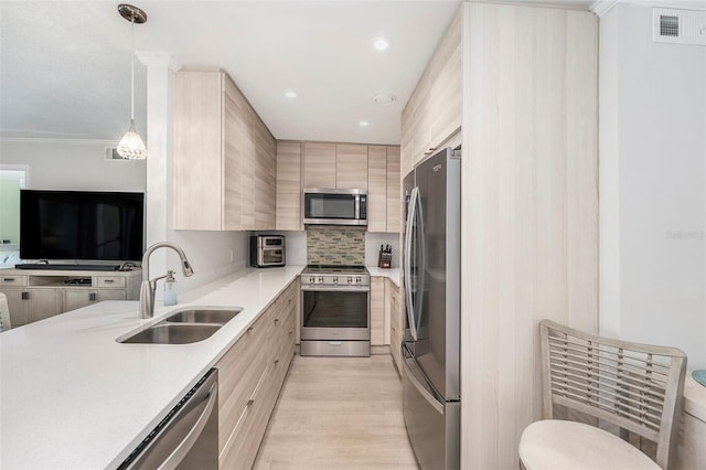 kitchen with visible vents, modern cabinets, light brown cabinetry, a sink, and appliances with stainless steel finishes