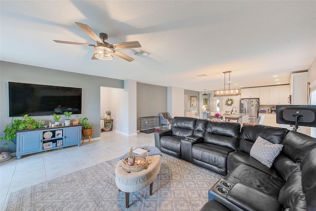 living room featuring light tile patterned flooring, visible vents, ceiling fan with notable chandelier, and baseboards