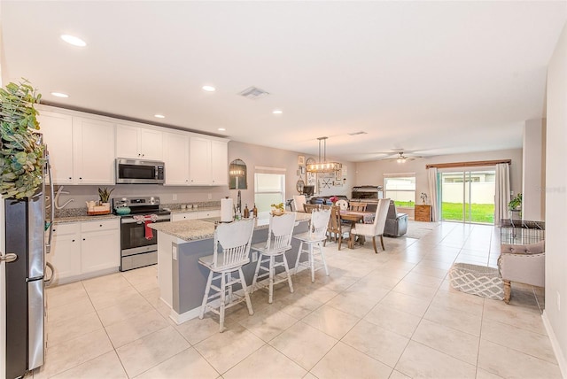 kitchen featuring white cabinets, light tile patterned flooring, a kitchen island with sink, and appliances with stainless steel finishes