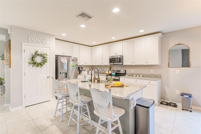 kitchen featuring visible vents, light tile patterned floors, a kitchen breakfast bar, white cabinets, and stainless steel appliances