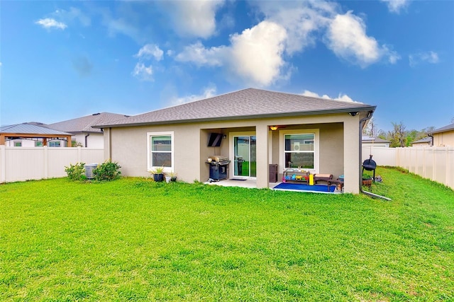 rear view of house featuring a shingled roof, a lawn, stucco siding, a fenced backyard, and a patio area