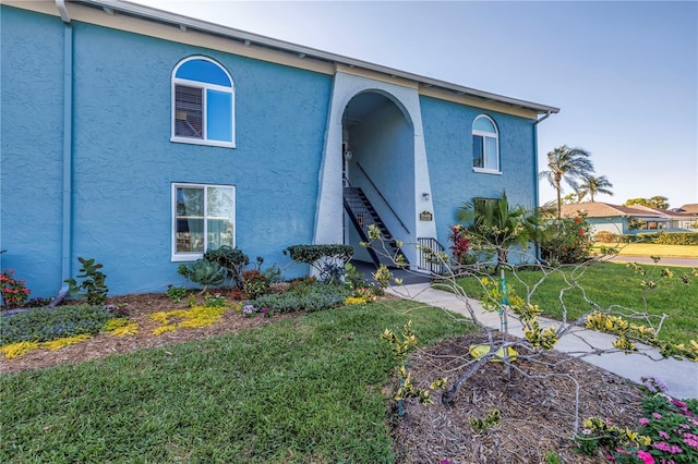 view of front facade featuring stucco siding, stairs, and a front lawn