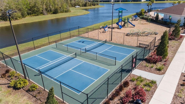 view of tennis court with playground community, fence, and a water view