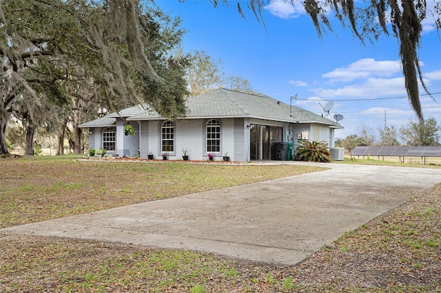 view of front facade with a front lawn, roof with shingles, central AC unit, stucco siding, and driveway