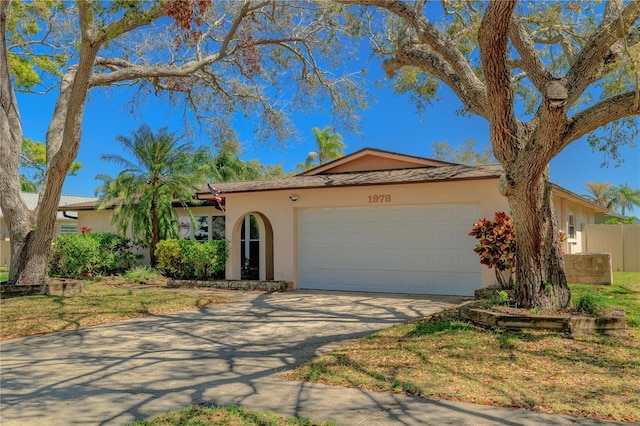 ranch-style house featuring stucco siding, driveway, an attached garage, and fence