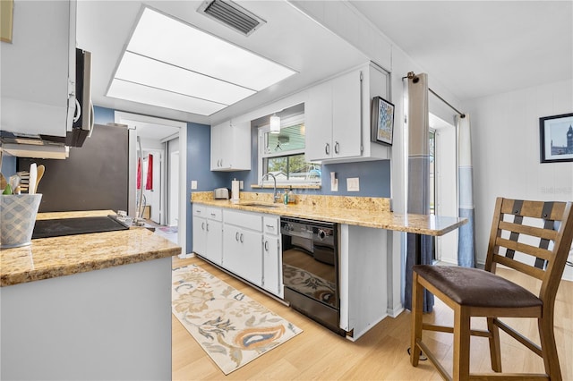 kitchen featuring visible vents, light wood-type flooring, a sink, black dishwasher, and white cabinetry