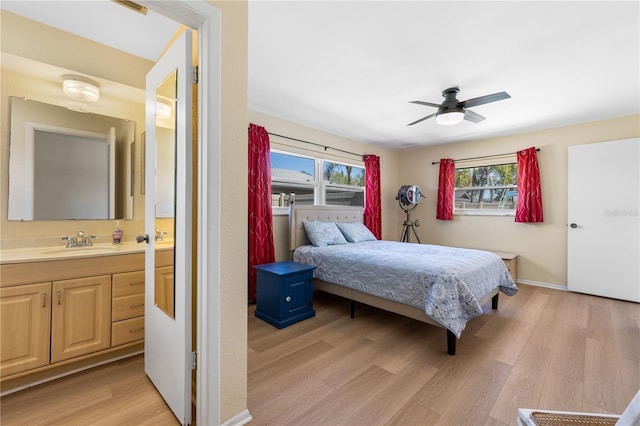 bedroom featuring light wood-style flooring, multiple windows, ensuite bathroom, and a sink