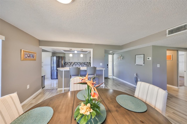 dining room featuring light wood-style flooring, visible vents, and a textured ceiling