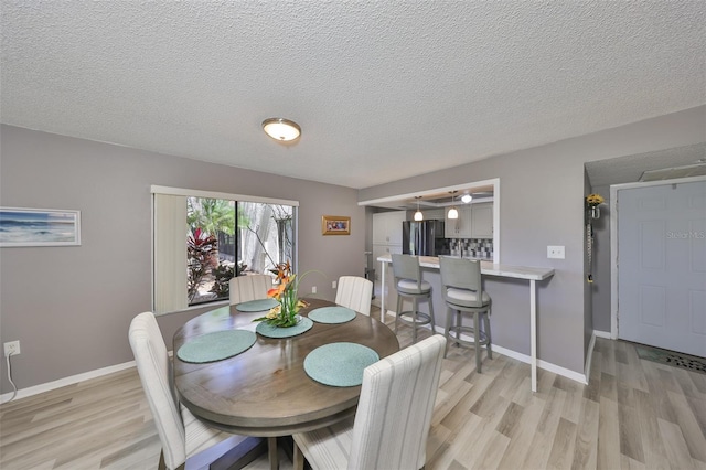 dining area featuring baseboards, a textured ceiling, and light wood finished floors