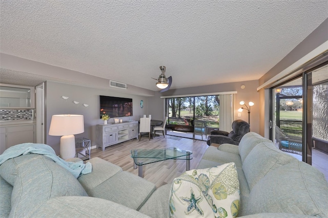 living room with light wood-type flooring, visible vents, and a textured ceiling