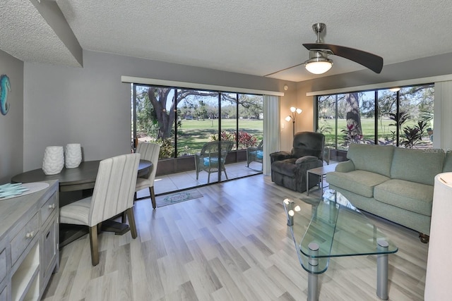 living room with ceiling fan, a textured ceiling, and light wood-style flooring