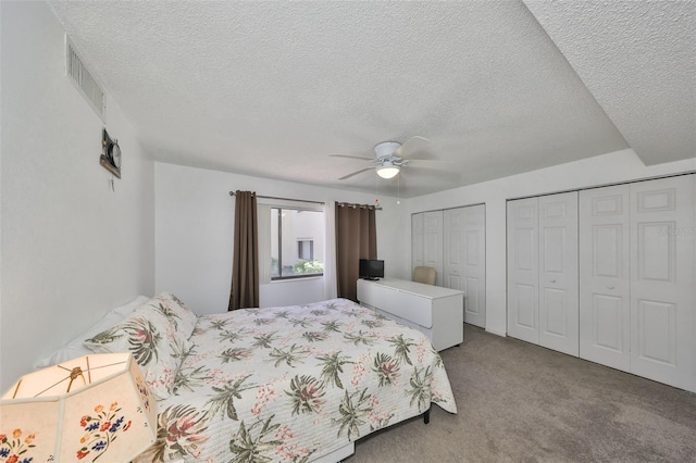 bedroom featuring visible vents, two closets, a textured ceiling, carpet floors, and ceiling fan