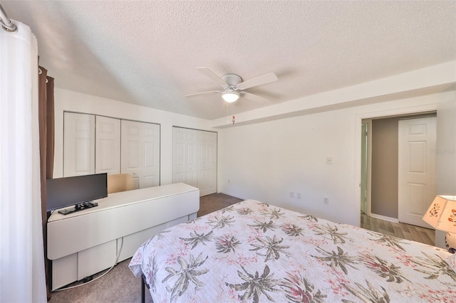 carpeted bedroom with ceiling fan, two closets, and a textured ceiling