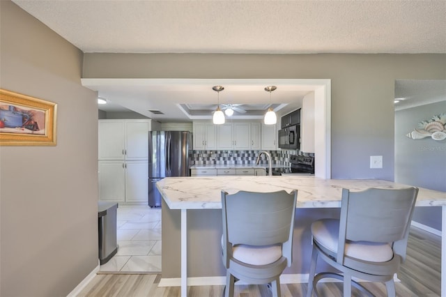 kitchen with black appliances, tasteful backsplash, a peninsula, a breakfast bar area, and a raised ceiling