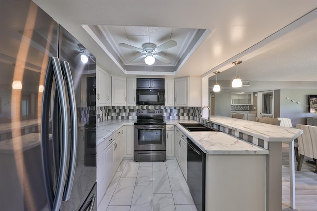 kitchen featuring a peninsula, a sink, black appliances, a raised ceiling, and tasteful backsplash