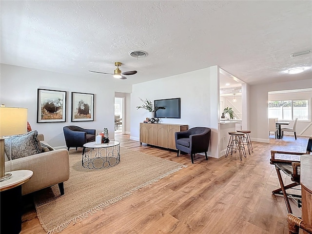 living room featuring baseboards, visible vents, light wood finished floors, and a textured ceiling