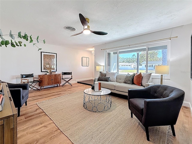 living area with light wood-type flooring, visible vents, a ceiling fan, a textured ceiling, and baseboards