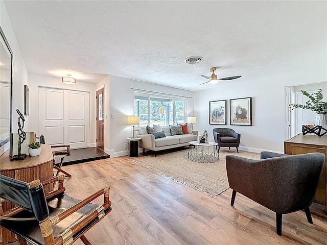 living room with visible vents, baseboards, light wood-style flooring, a textured ceiling, and a ceiling fan