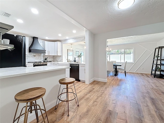 kitchen with a kitchen bar, visible vents, custom range hood, stainless steel range with electric cooktop, and dishwashing machine