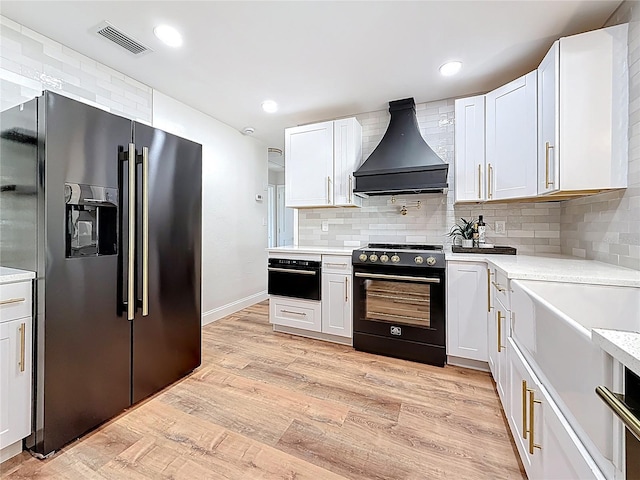 kitchen featuring premium range hood, visible vents, black appliances, light wood-style flooring, and light countertops