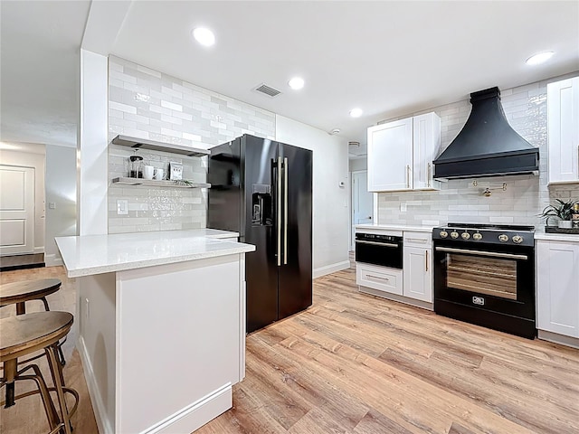 kitchen with visible vents, premium range hood, decorative backsplash, light wood-style flooring, and black appliances