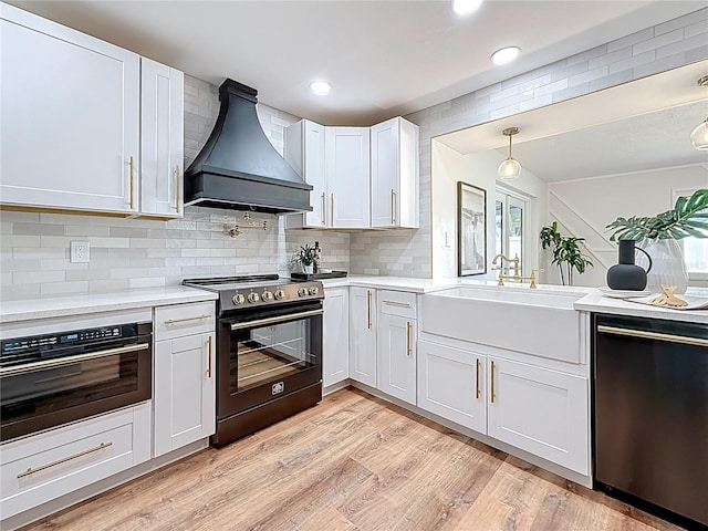 kitchen with premium range hood, light countertops, light wood-style flooring, black appliances, and a sink